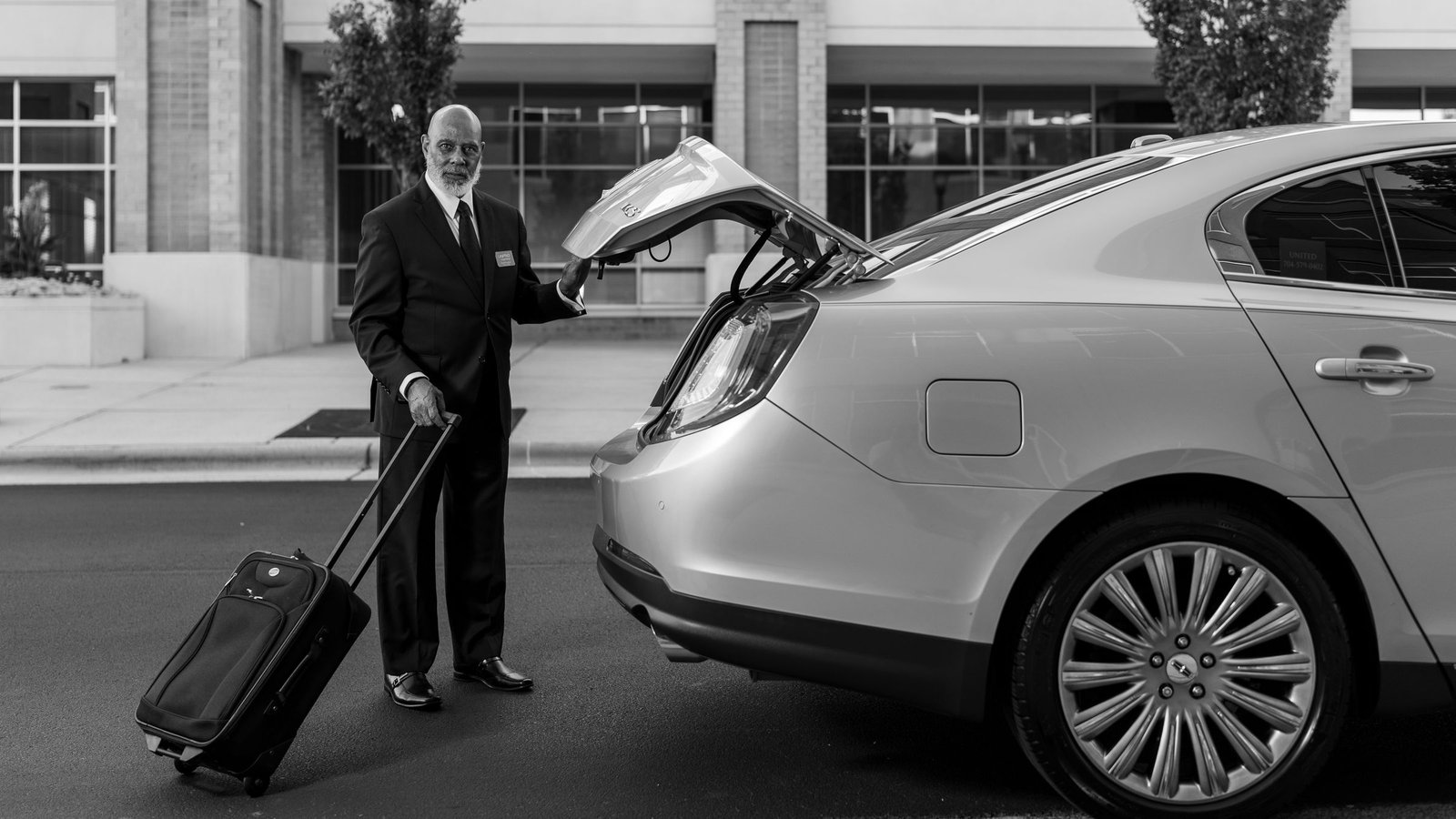 Professional chauffeur loading passenger luggage into a private transfer car